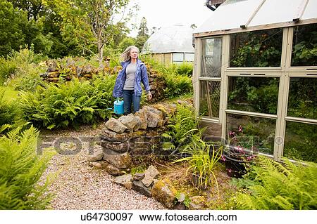 Mature woman carrying watering can in garden View Large Photo Image Stock Photo - Mature woman carrying watering can in garden. Fotosearch
