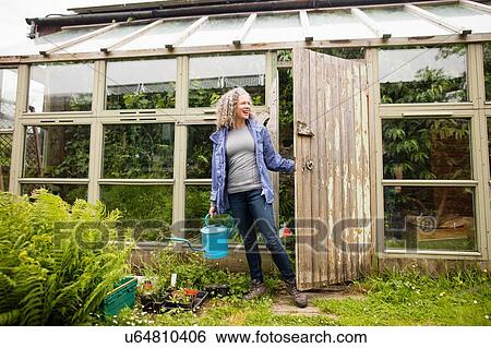 Mature woman carrying watering can opening greenhouse View Large Photo Image Stock Photograph - Mature woman carrying watering can opening greenhouse. Fotosearch