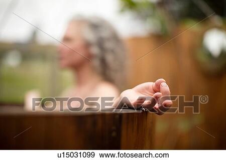 Stock Photo - Mature woman meditating in hot tub at eco retreat. Fotosearch