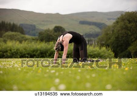 Stock Photography - Mature woman practicing yoga backward bend in field. Fotosearch