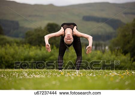 Picture - Mature woman practicing yoga bending backward in field. Fotosearch