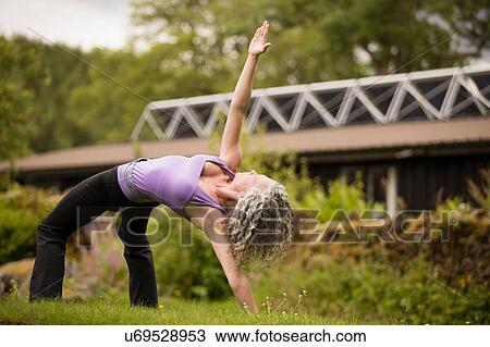 Stock Image - Mature woman practicing yoga bridge pose in eco lodge garden. Fotosearch