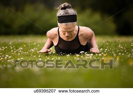 Stock Photo - Mature woman practicing yoga cobra pose in field. Fotosearch