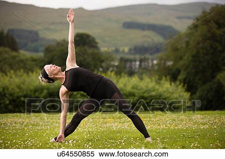 Stock Photography - Mature woman practicing yoga cow face pose in field. Fotosearch