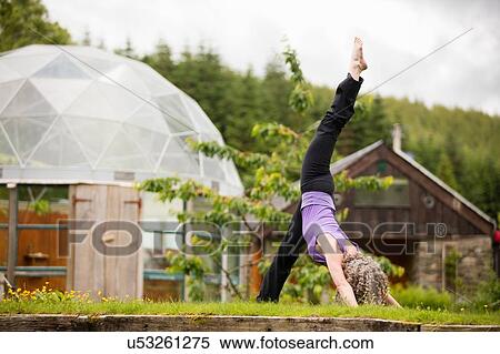Stock Photography - Mature woman practicing yoga with leg raised in eco lodge garden. Fotosearch