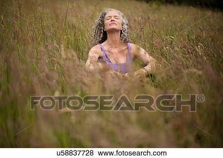Stock Photo - Mature woman sitting in long grass meditating. Fotosearch