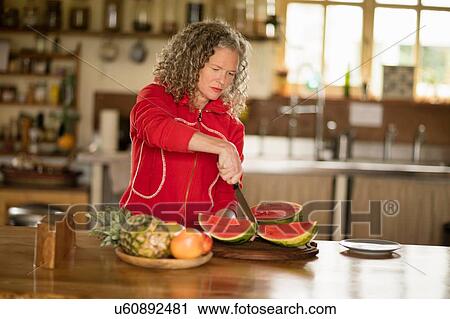 Mature woman slicing watermelon in kitchen View Large Photo Image Stock Image - Mature woman slicing watermelon in kitchen. Fotosearch