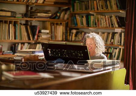 Mature woman smiling whilst playing piano in living room View Large Photo Image Stock Photo - Mature woman smiling whilst playing piano in living room. Fotosearch