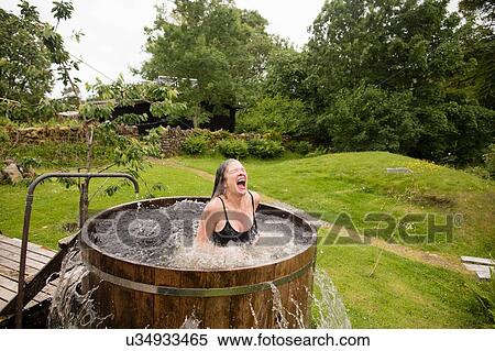 Stock Photography - Mature woman splashing in fresh cold water tub at eco retreat. Fotosearch