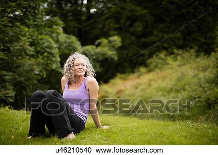 Stock Image - Mature woman taking a break from yoga practice in field. Fotosearch