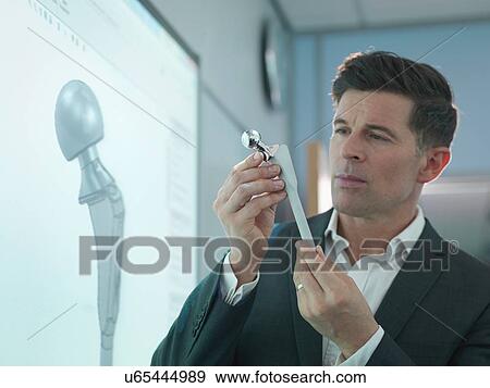 Stock Photo - Medical product designer inspecting hip joint model with graphical screen. Fotosearch