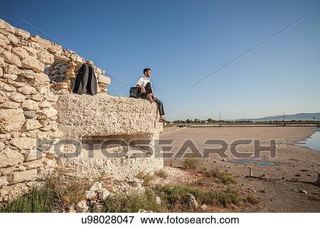 Stock Photo - Mid adult business man looking out at sea from beach wall. Fotosearch