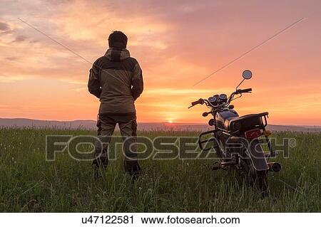 Mid adult man, standing in field, next to motorbike, at sunset, rear view View Large Photo Image Stock Image - Mid adult man, standing in field, next to motorbike, at sunset, rear view. Fotosearch