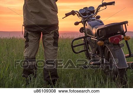 Mid adult man, standing in field, next to motorbike, at sunset, rear view, low section View Large Photo Image Stock Photo - Mid adult man, standing in field, next to motorbike, at sunset, rear view, low section. Fotosearch