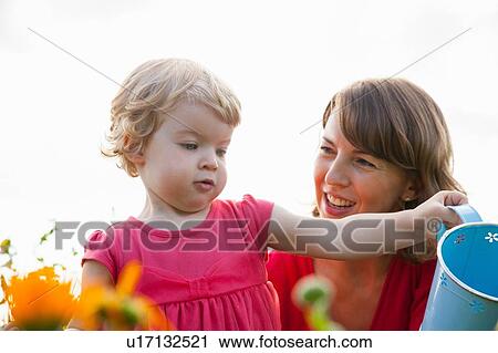 Mid adult mother and toddler daughter watering flowers in field View Large Photo Image Stock Image - Mid adult mother and toddler daughter watering flowers in field. Fotosearch