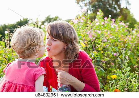 Mid adult mother and toddler daughter kissing in flower field View Large Photo Image Stock Image - Mid adult mother and toddler daughter kissing in flower field. Fotosearch