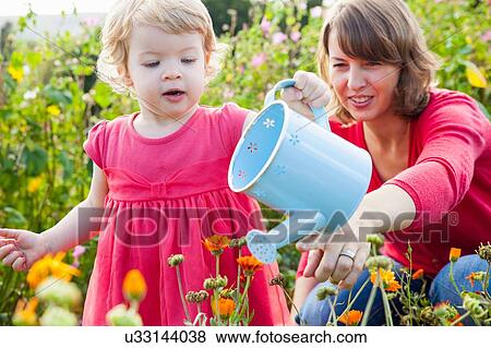 Stock Photo - Mid adult mother and toddler daughter watering flower field. Fotosearch