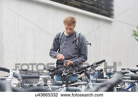Stock Image - Mid adult using key to lock, unlock bicycle lock, looking down. Fotosearch