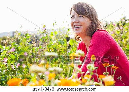 Mid adult woman crouching in flower field View Large Photo Image Stock Image - Mid adult woman crouching in flower field. Fotosearch