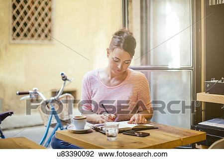Mid adult woman sitting at table writing in notebook View Large Photo Image Stock Image - Mid adult woman sitting at table writing in notebook. Fotosearch
