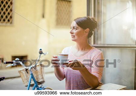 Mid adult woman sitting at table holding cup and saucer, looking away View Large Photo Image Stock Photograph - Mid adult woman sitting at table holding cup and saucer, looking away. Fotosearch