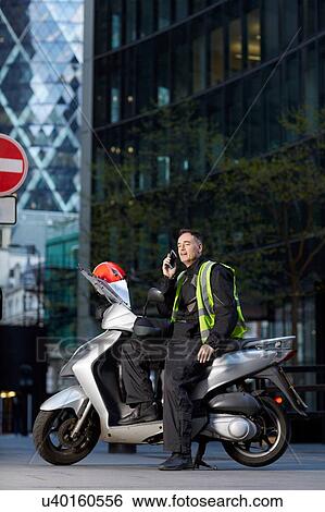 Stock Photograph - Motor scooter rider talking on smartphone in London. Fotosearch