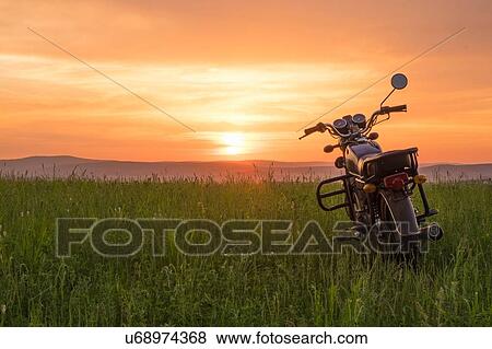 Stock Photo - Motorbike parked on grass, at sunset, Sarsy, Sverdlovsk region, Russia. Fotosearch
