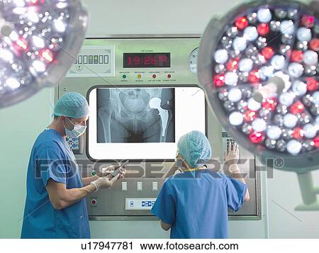 Stock Image - Orthopaedic surgeon and nurse with replacement hip stem in operating theatre. Fotosearch
