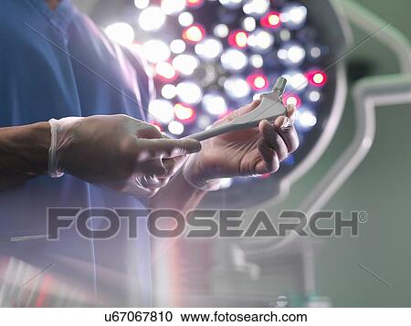Stock Image - Orthopaedic surgeon in operating theatre with replacement hip stem, close up. Fotosearch
