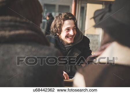 Stock Image - Over the shoulder view of young adult friends talking in cafe. Fotosearch