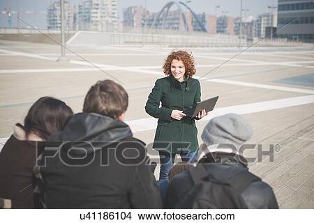 Picture - Over the shoulder view of young woman using laptop in front of friends. Fotosearch