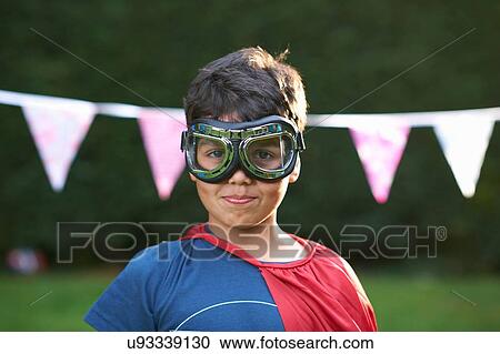 Stock Image - Portrait of boy wearing goggles and cape, looking at camera. Fotosearch