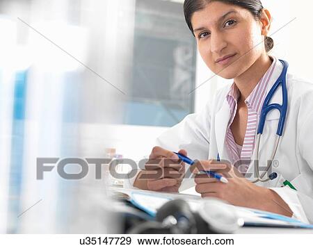 Portrait of female doctor at desk working on medical records View Large Photo Image Stock Photo - Portrait of female doctor at desk working on medical records. Fotosearch