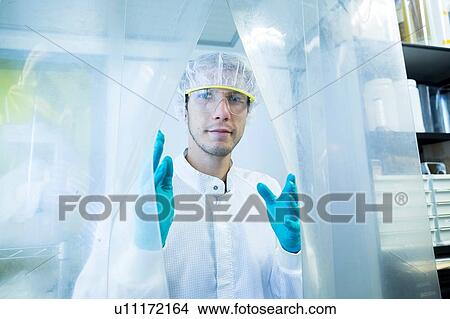 Picture - Portrait of male scientist behind plastic curtain in lab cleanroom. Fotosearch