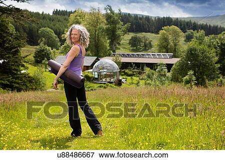 Portrait of mature woman carrying yoga mat in field at eco lodge View Large Photo Image Stock Photo - Portrait of mature woman carrying yoga mat in field at eco lodge. Fotosearch