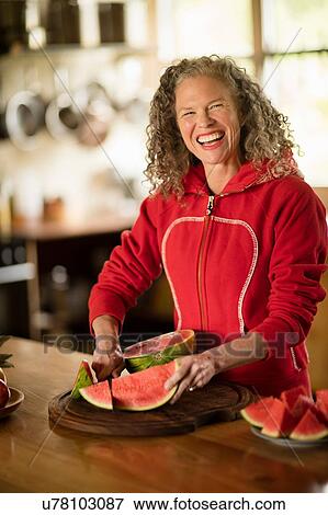 Stock Photo - Portrait of mature woman slicing watermelon in kitchen. Fotosearch
