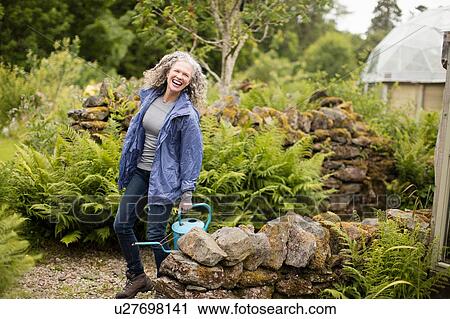 Stock Image - Portrait of mature woman with watering can in garden. Fotosearch