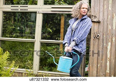 Portrait of mature woman with watering can leaning against greenhouse View Large Photo Image Stock Image - Portrait of mature woman with watering can leaning against greenhouse. Fotosearch
