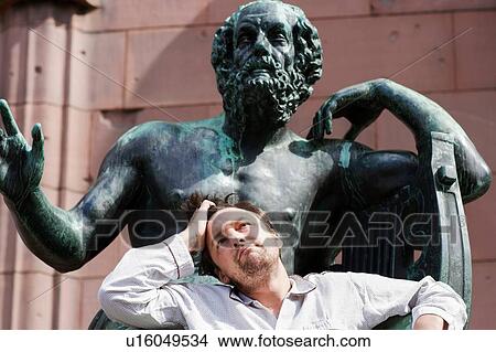 Picture - Portrait of mid adult man with hand in hair in front of sculpture, Freiburg, Baden, Germany. Fotosearch