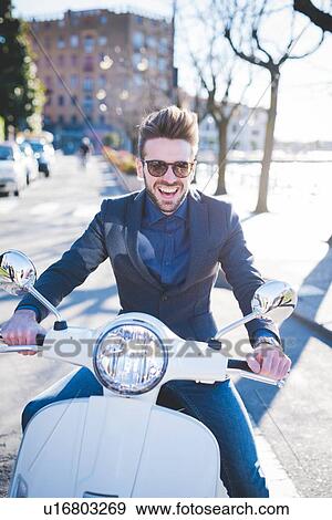 Stock Photo - Portrait of smiling young man sitting on moped at roadside. Fotosearch