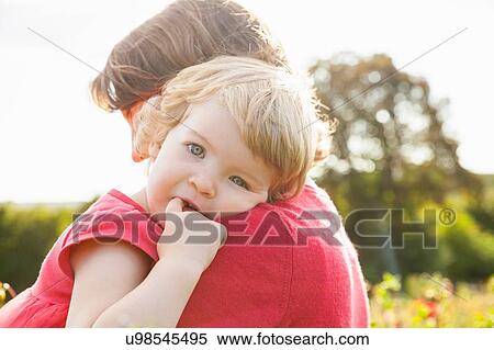 Stock Photography - Portrait of toddler daughter resting on mothers shoulder in flower field. Fotosearch