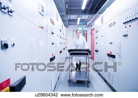 Stock Image - Portrait of young female scientist pushing trolley in technical room. Fotosearch