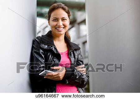 Portrait of young woman holding smartphone leaning against pillar View Large Photo Image Stock Photo - Portrait of young woman holding smartphone leaning against pillar. Fotosearch