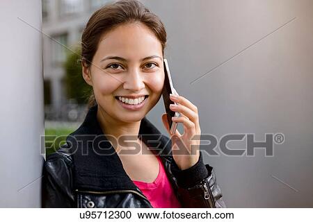 Portrait of young woman leaning against pillar talking on smartphone View Large Photo Image Stock Image - Portrait of young woman leaning against pillar talking on smartphone. Fotosearch
