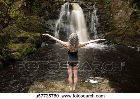 Rear view of mature woman practicing with open arms in front of waterfall View Large Photo Image Stock Image - Rear view of mature woman practicing with open arms in front of waterfall. Fotosearch