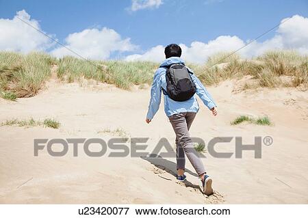 Stock Photo - Rear view of mid adult female walker, walking up sand dune. Fotosearch