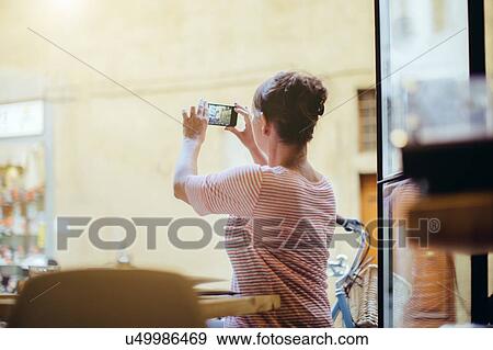 Stock Photo - Rear view of mid adult woman sitting using smartphone to take photograph. Fotosearch