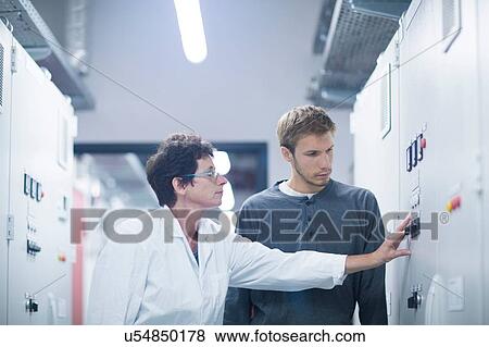 Stock Photo - Scientist and technician pressing switch in technical room. Fotosearch
