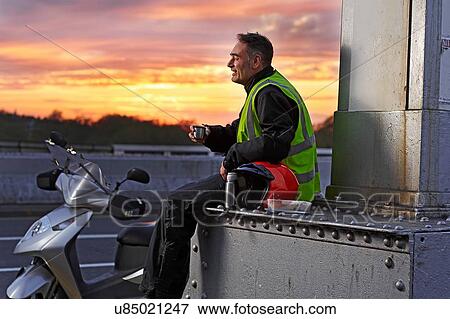 Stock Photo - Scooter rider taking a break on city bridge at sunset. Fotosearch