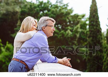 Stock Image - Senior couple leaning on wall, looking at view. Fotosearch